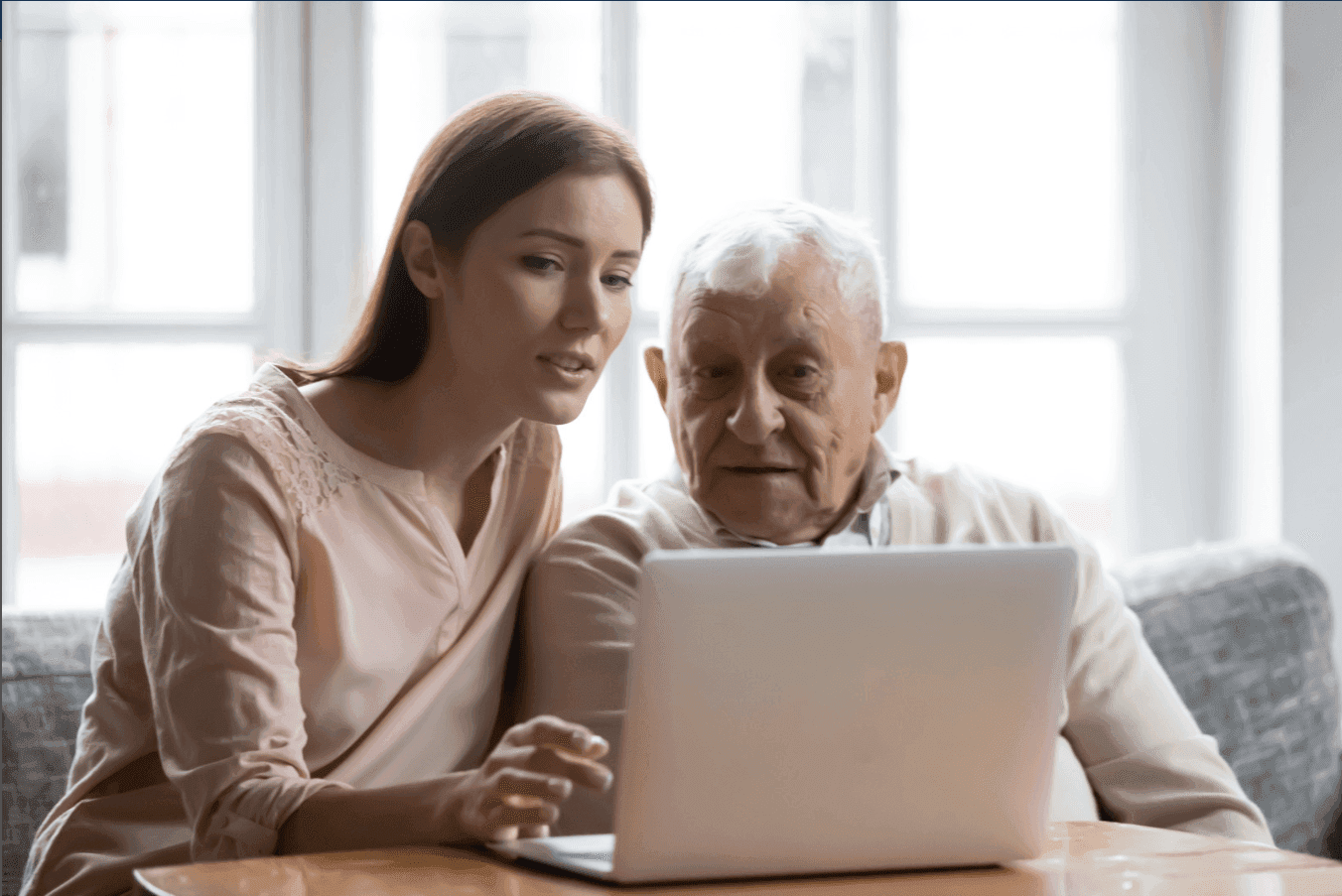 A young adult daughter sits with her elderly father at a laptop, helping him review senior living options together, a moment of care and collaboration.