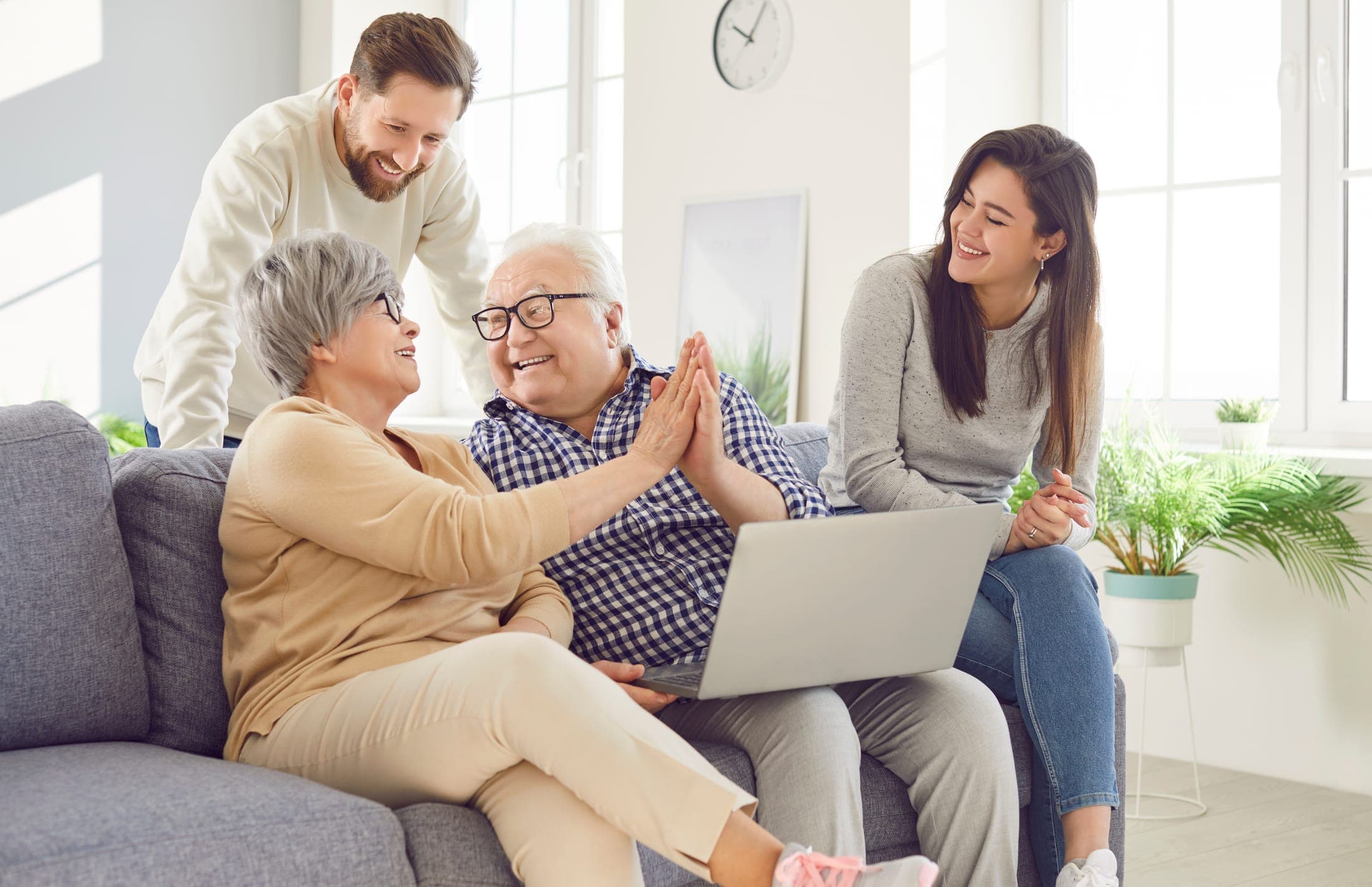 Adult children gather around their parents on a couch, discovering senior living options together on a laptop: a moment of relief and family connection.