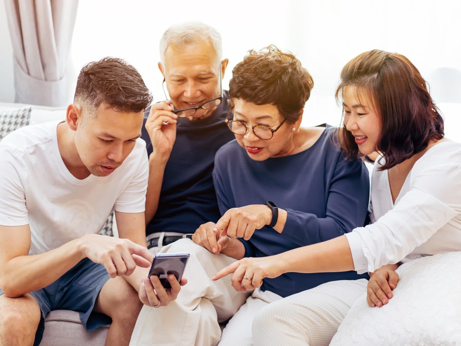 An adult son and daughter with their two parents, all leaning in together over a phone, working through a Senior Living decision as a family.